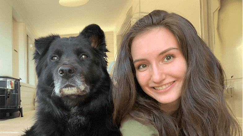 University of Arizona student Mia Hickey smiles while next to her black dog