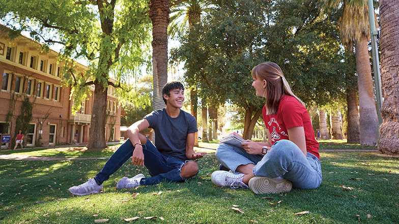 University of Arizona students sitting on the grass on campus.