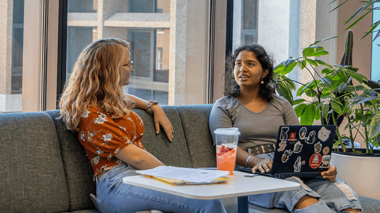 Two University of Arizona students are seated on a couch engaged in conversation.