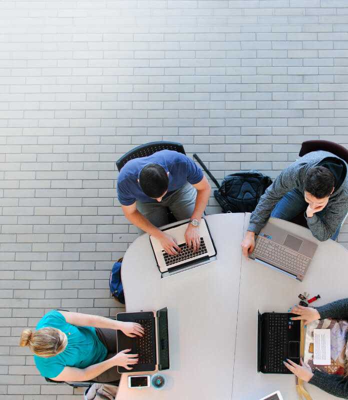 Top view of students working on laptops on table.