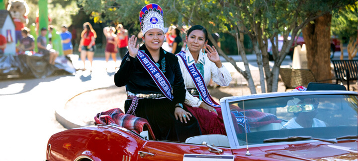 Pageant contestants sitting in a convertible car waving at Wildcat fans during the homecoming parade.
