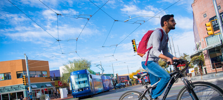 Student riding a bicycle downtown in Tucson, Arizona next to the street car.