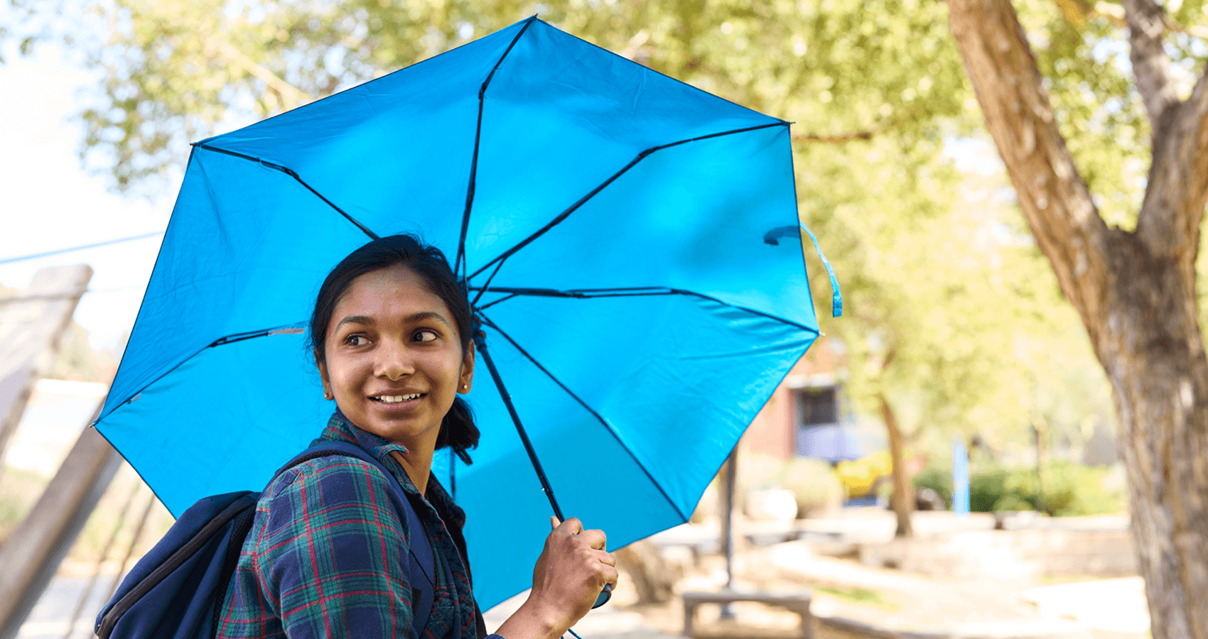 Student touring campus with an umbrella on a sunny day
