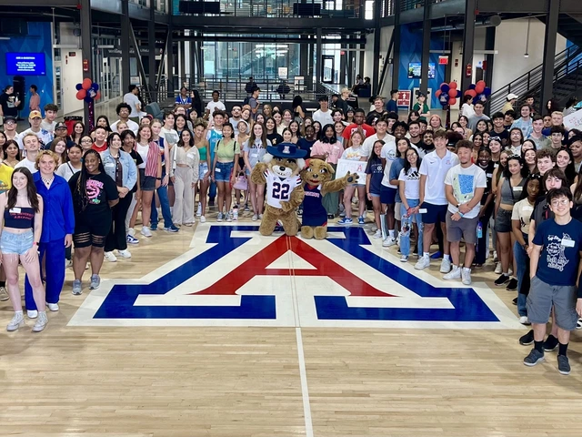 A group of students stand on a basketball court around a large block "A"