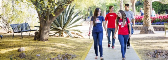 Arizona students walking on campus path near flowers and a shady tree