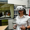 A woman wearing a white button-down shirt uses a virtual reality headset and handheld controllers inside the Lundgren Consumer Science Lab. A large screen behind her displays a virtual retail space, and shelves of mugs and a red "U of A" shirt are visible in the background.